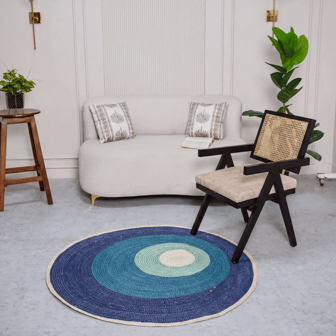 a cozy living room with a white sofa, a wooden stool, a woven chair, and a blue and white rug on the floor.