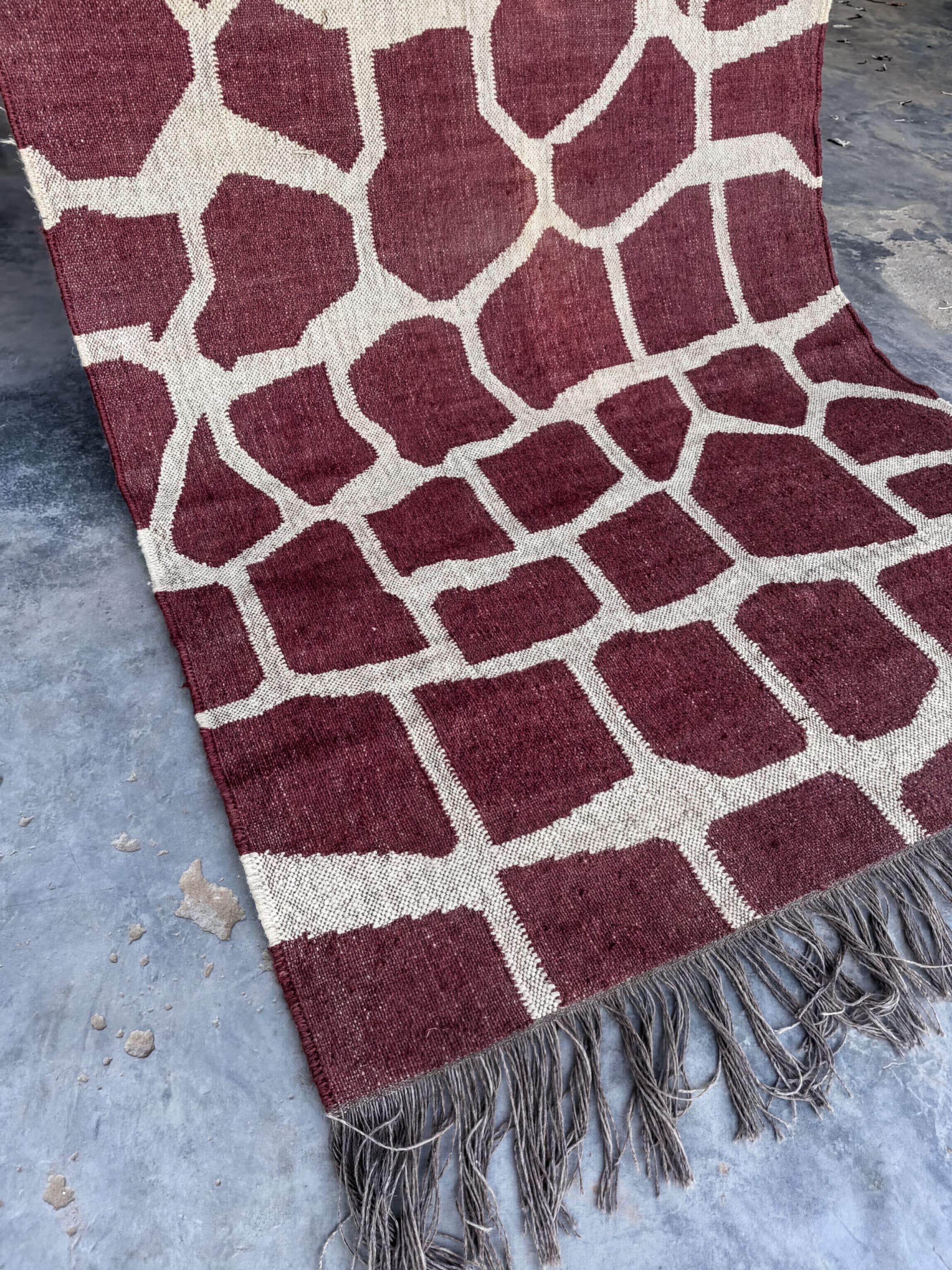 a close-up view of a red and white patterned rug with a fringed edge, placed on a concrete floor.