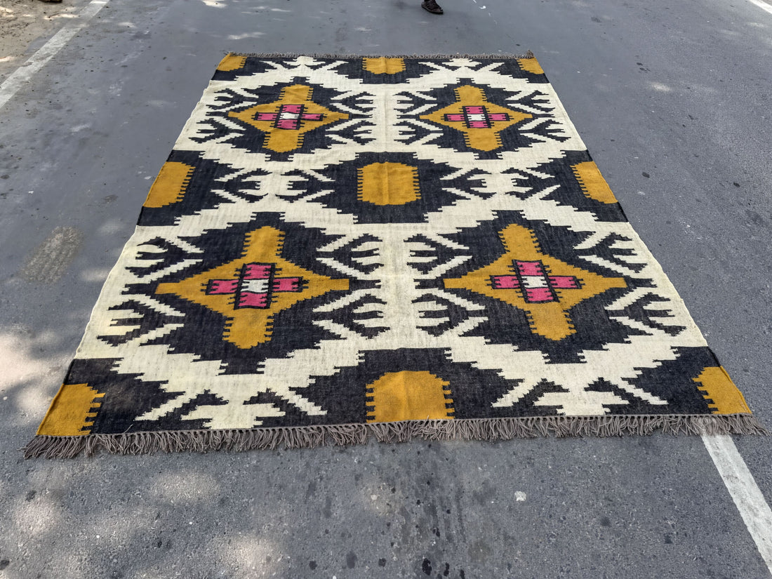 A large, colorful rug with a geometric pattern in shades of yellow, black, and white is spread out on the ground.
