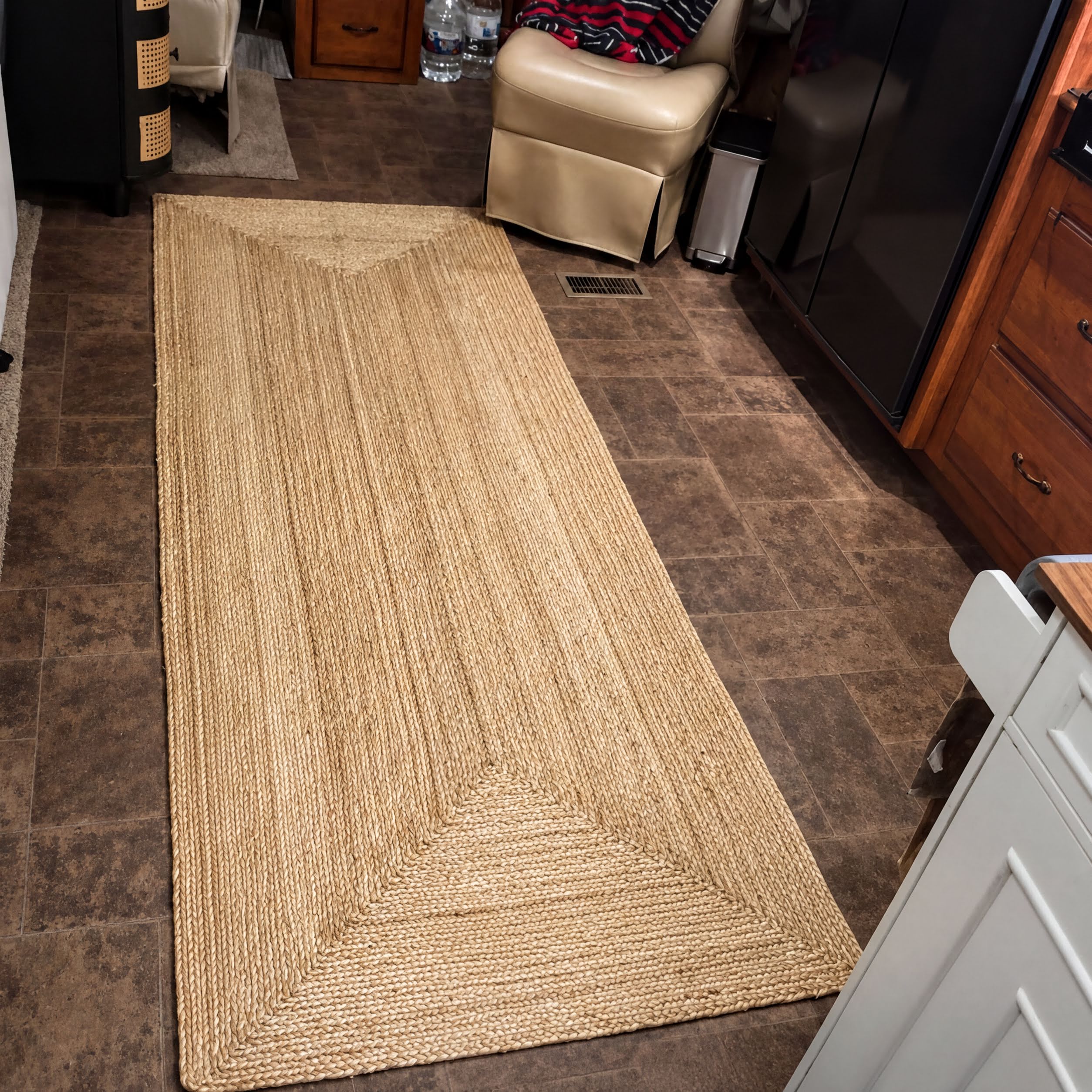 a room with a large rug on the floor, a wooden cabinet, a chair, and a refrigerator.